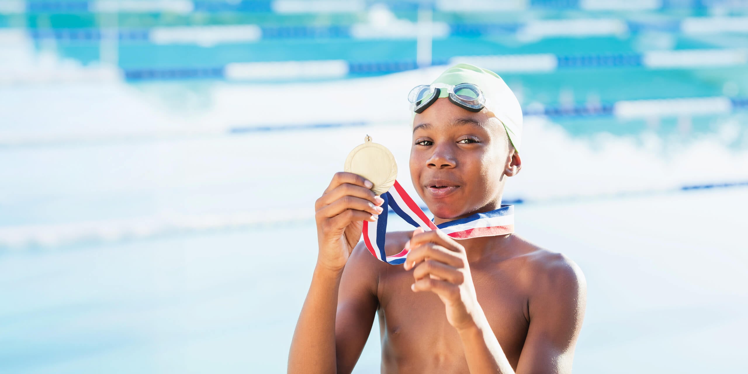 Boy at swimming pool holding up gold medal