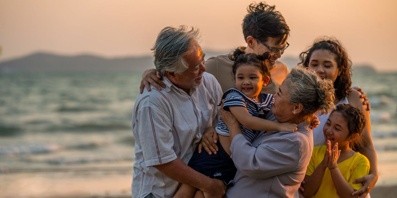 Multigeneration family embracing while standing on a shoreline.