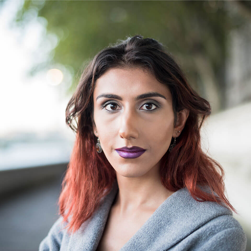 Portrait of contented transgender female with blurred park or riverwalk in background.