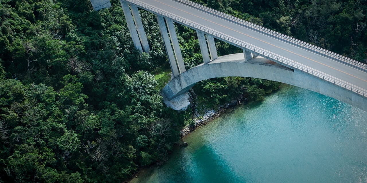 Drone image of a paved bridge extending over a wide, clear river