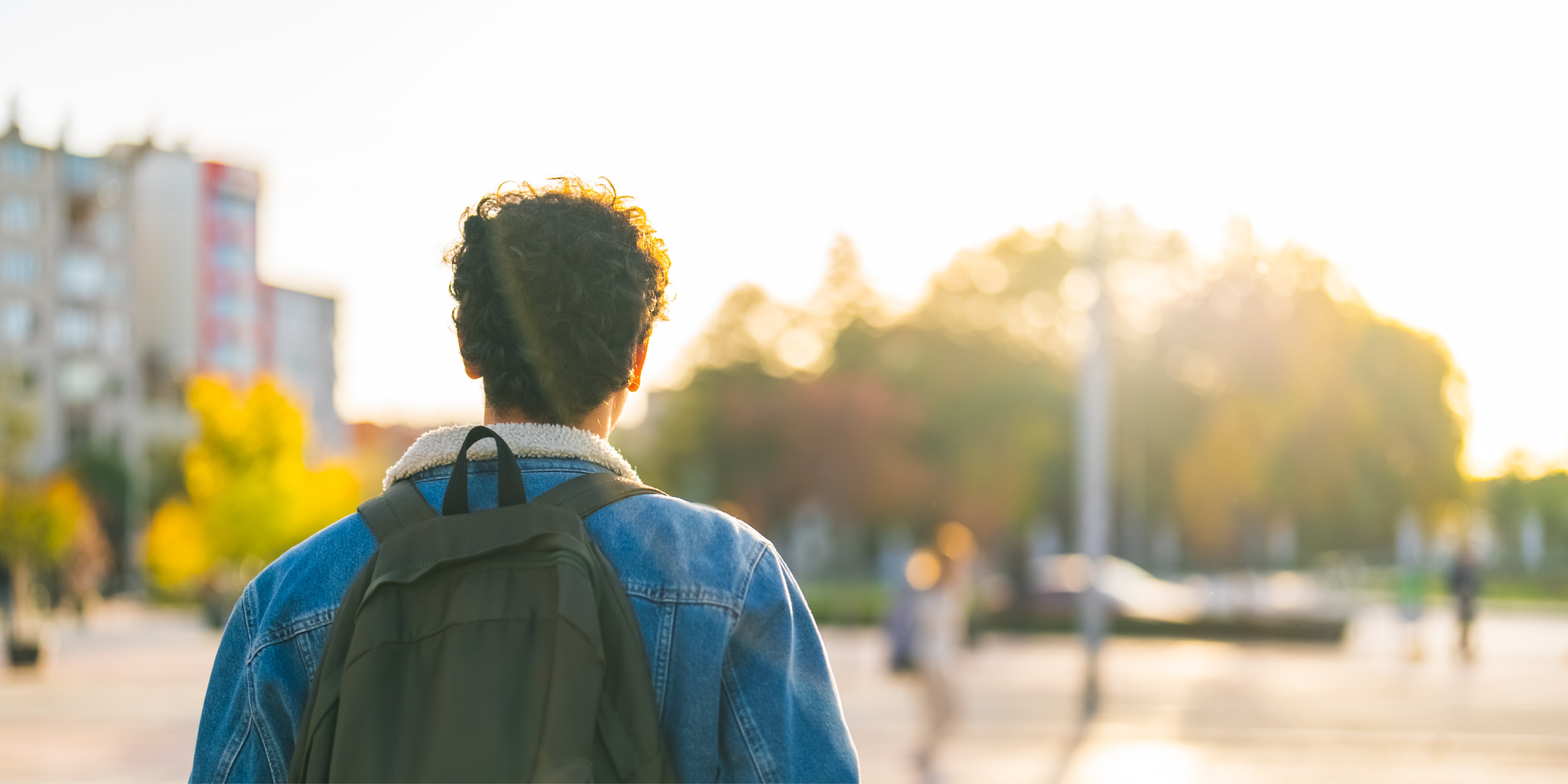 Photo of the back of a college student wearing a backpack looking into the distance. 