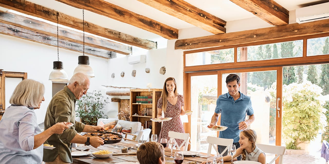 Family gathered around a dining table in a bright room with wooden beams and large windows.