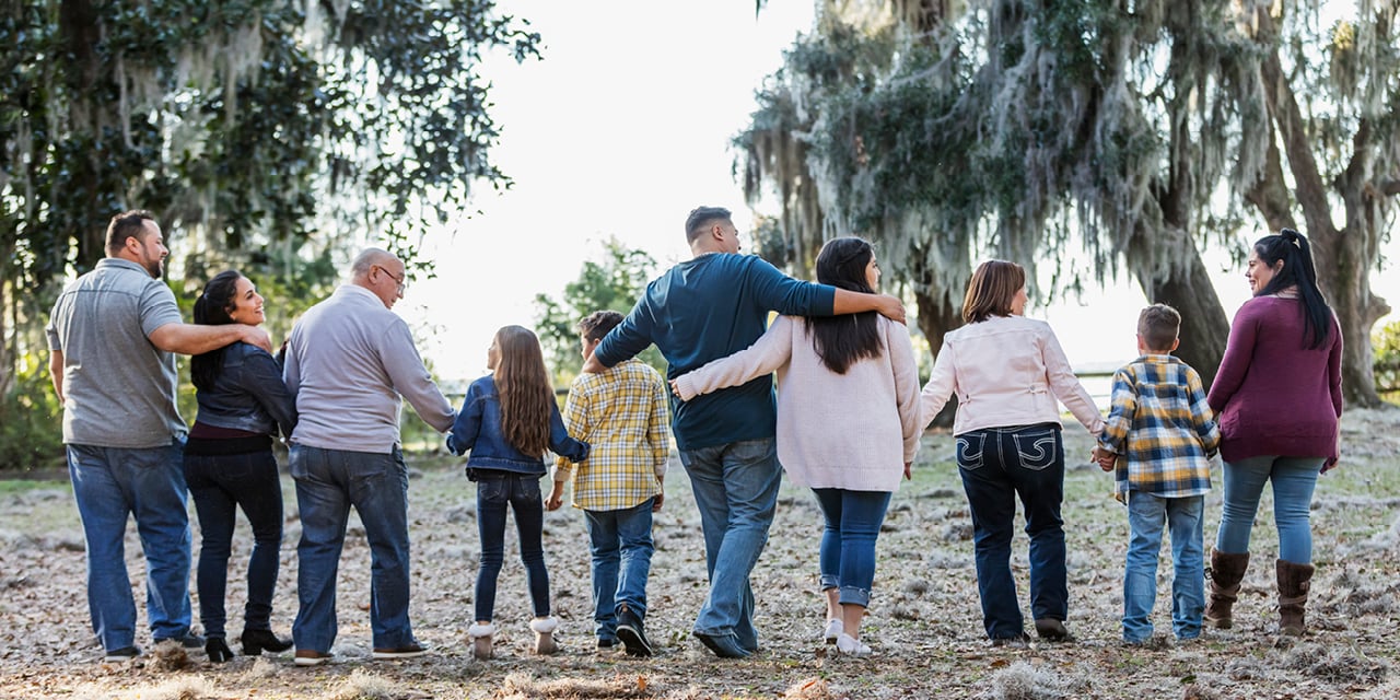Group of people walking outdoors, holding hands in a line with trees in the background.