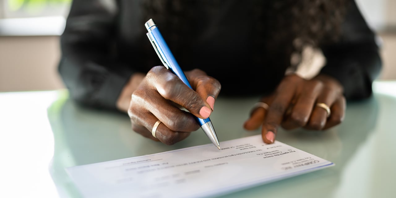 Closeup image of a person using a blue pen to sign a check.