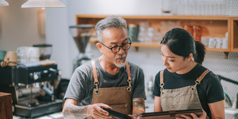 Man and woman in a workshop looking at a book while wearing work aprons