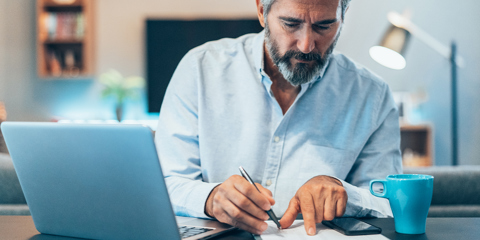 A man reviews papers as he sits at a desk with a computer.