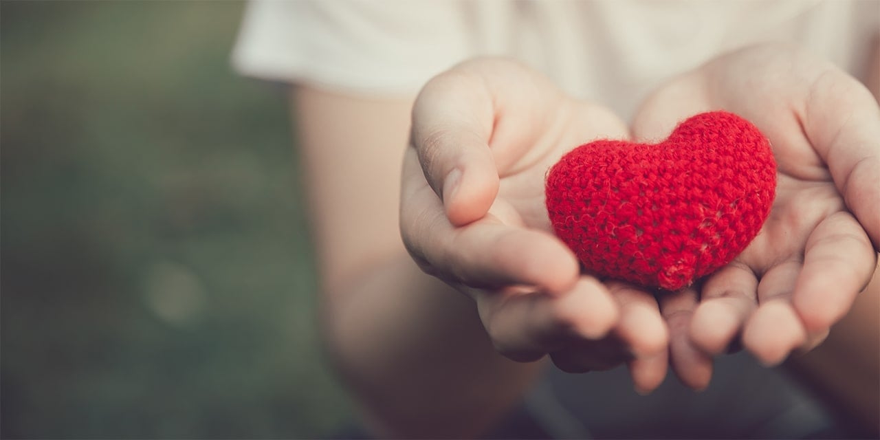 Outstretched hands holding a red crocheted heart.
