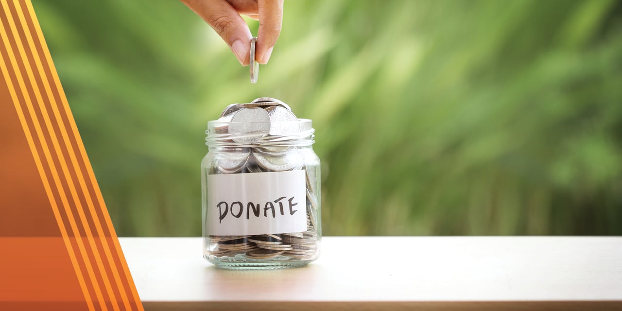 Hand dropping coins into a jar with the words donate on the front.