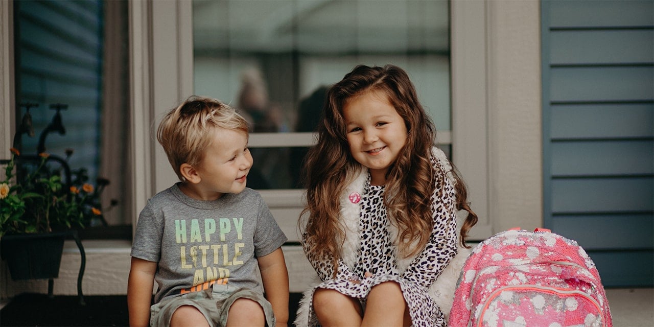 Young boy and girl smiling and sitting on front porch.