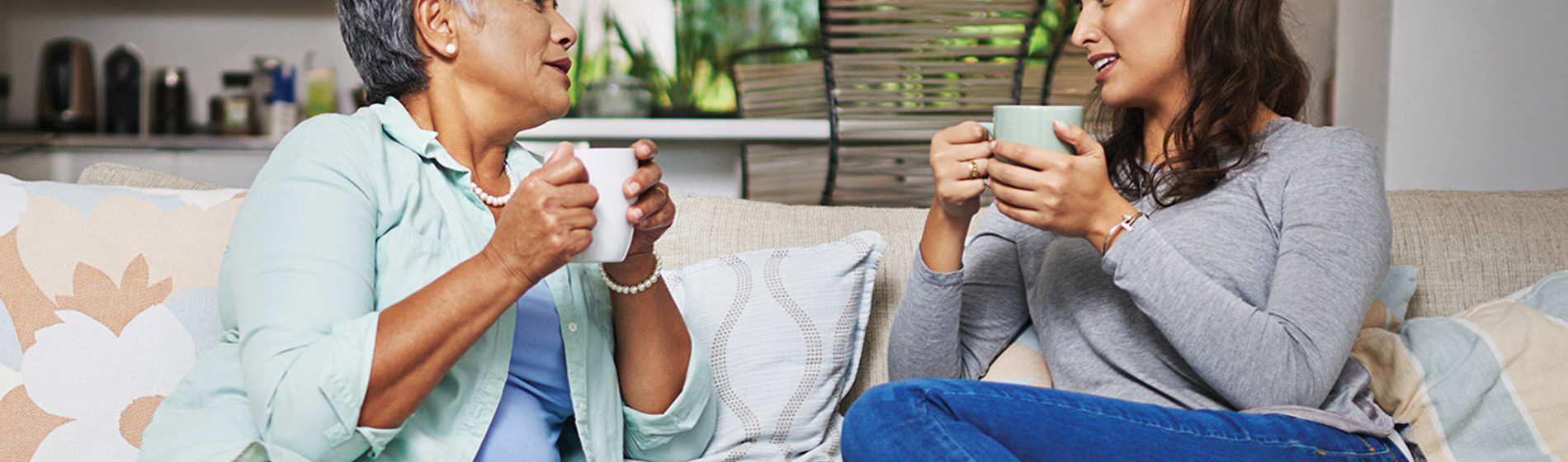 Mom and daughter sitting on sofa talking and drinking coffee.