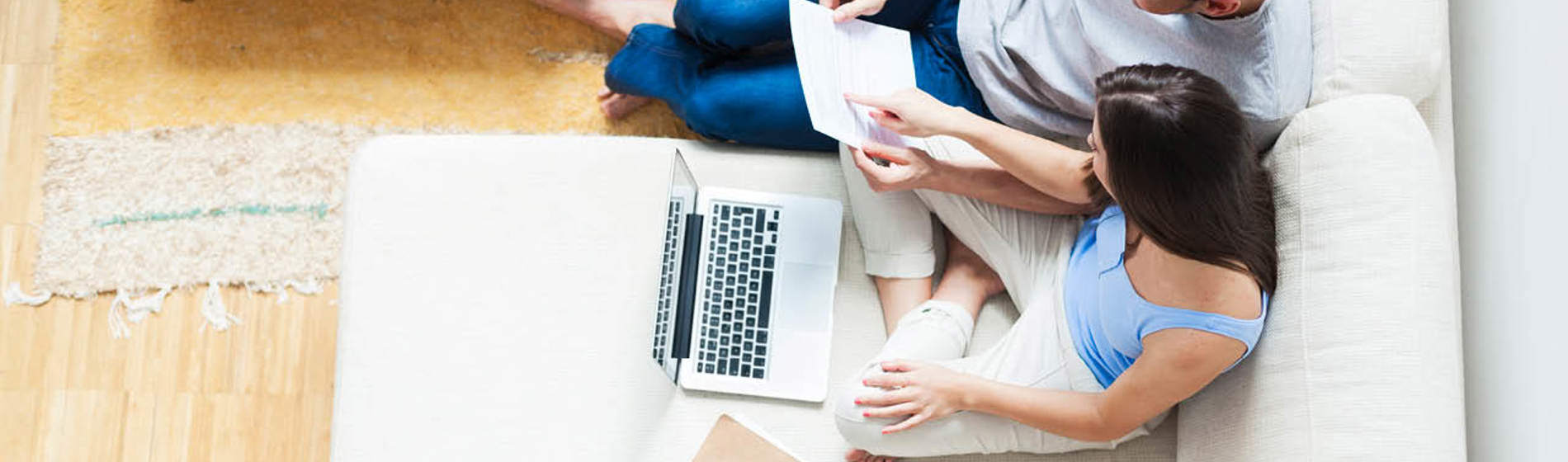 A couple sitting on a couch, reviewing a document together in front of a laptop, calculator, and other files.