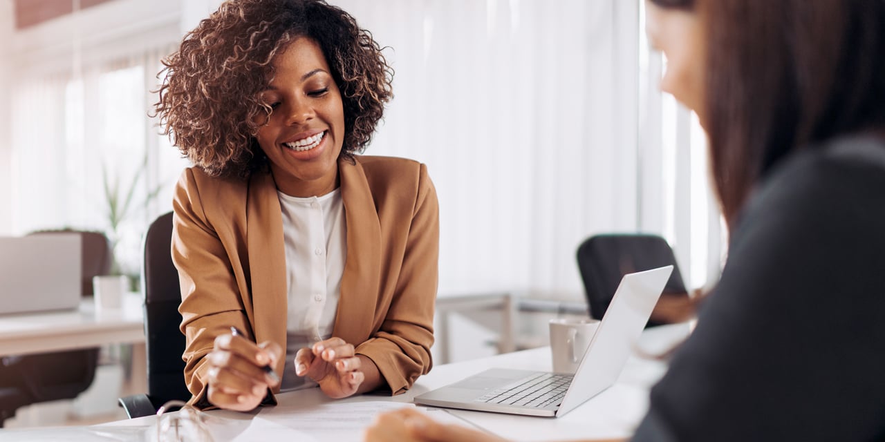 Two women at a business meeting sitting at a table with a laptop computer.