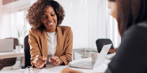 Two women at a business meeting sitting at a table with a laptop computer.