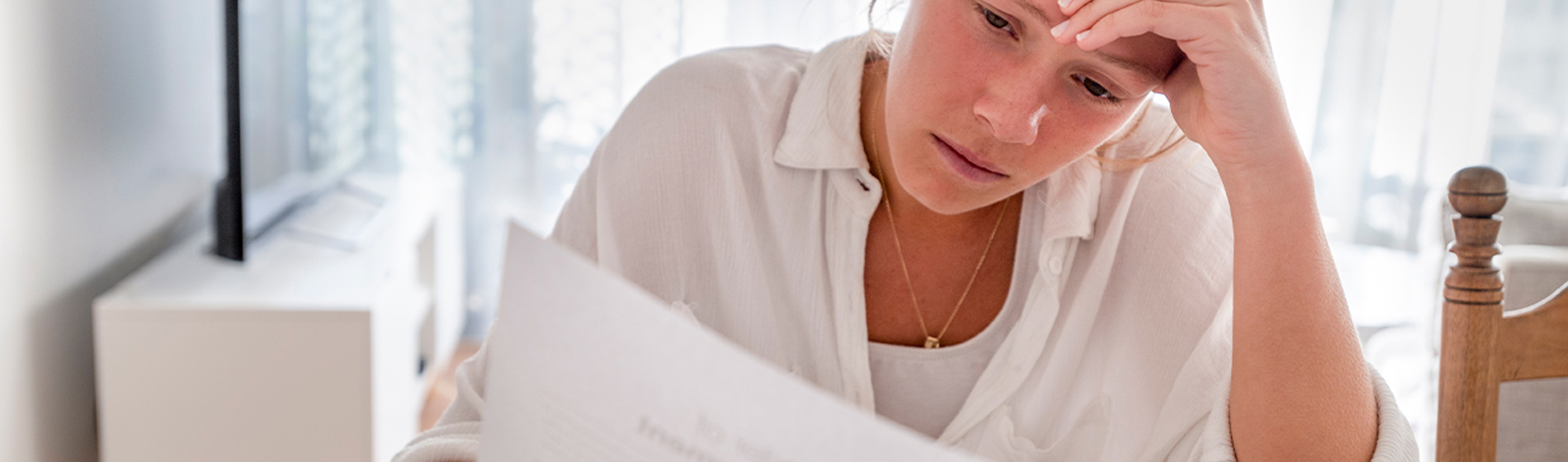 Woman stressed over paperwork sitting at table.