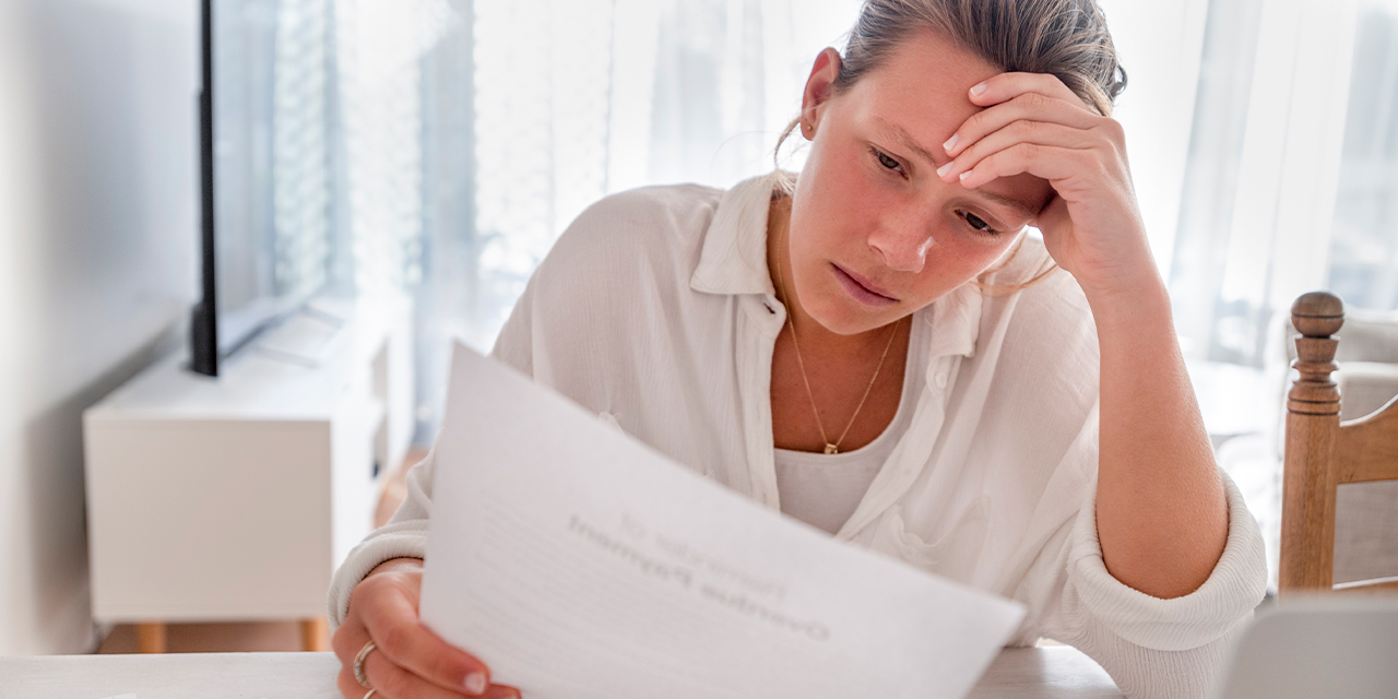Woman stressed over paperwork sitting at table.