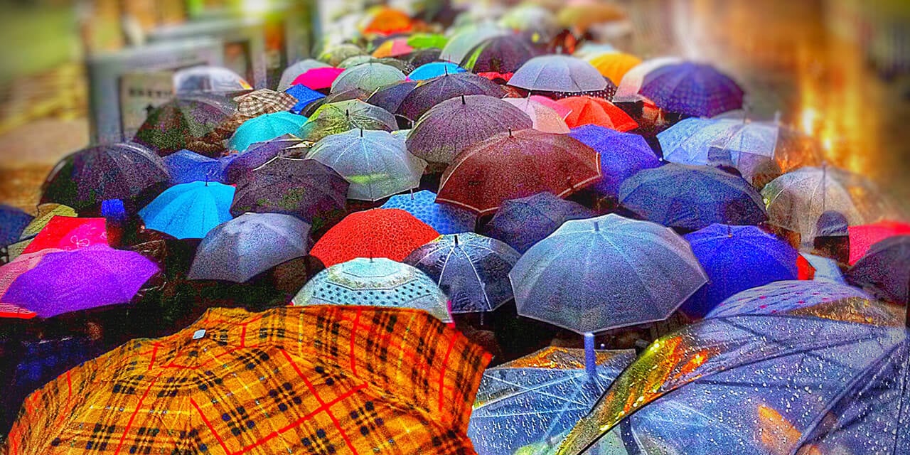 Large group of open, colorful umbrellas in an urban setting on a rainy day.