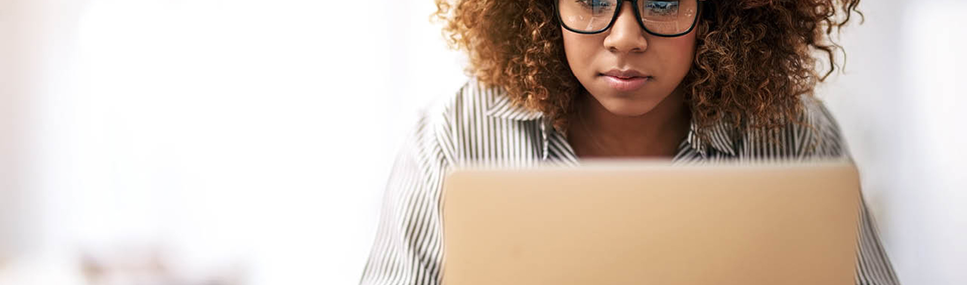 Woman wearing glasses sitting down working on a laptop.