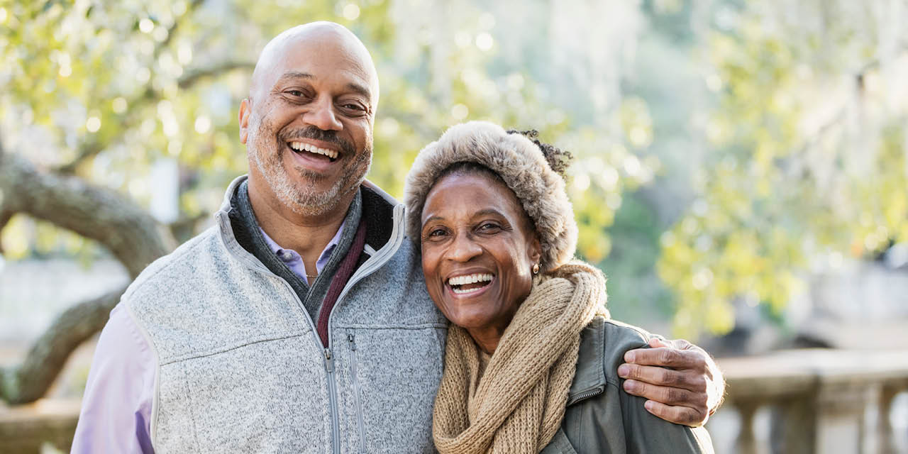Middle-aged couple smiling while standing in a park.