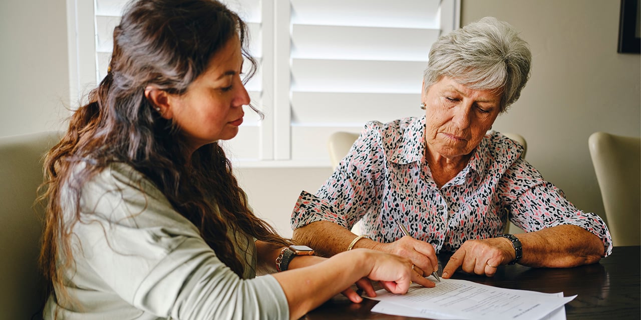 Elderly parent and child sitting at table reviewing paperwork