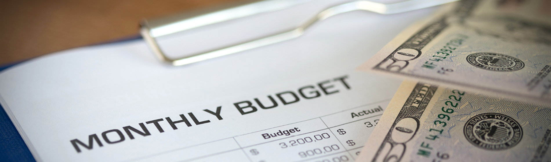 Monthly budget planning worksheet and cash connected to a clipboard 