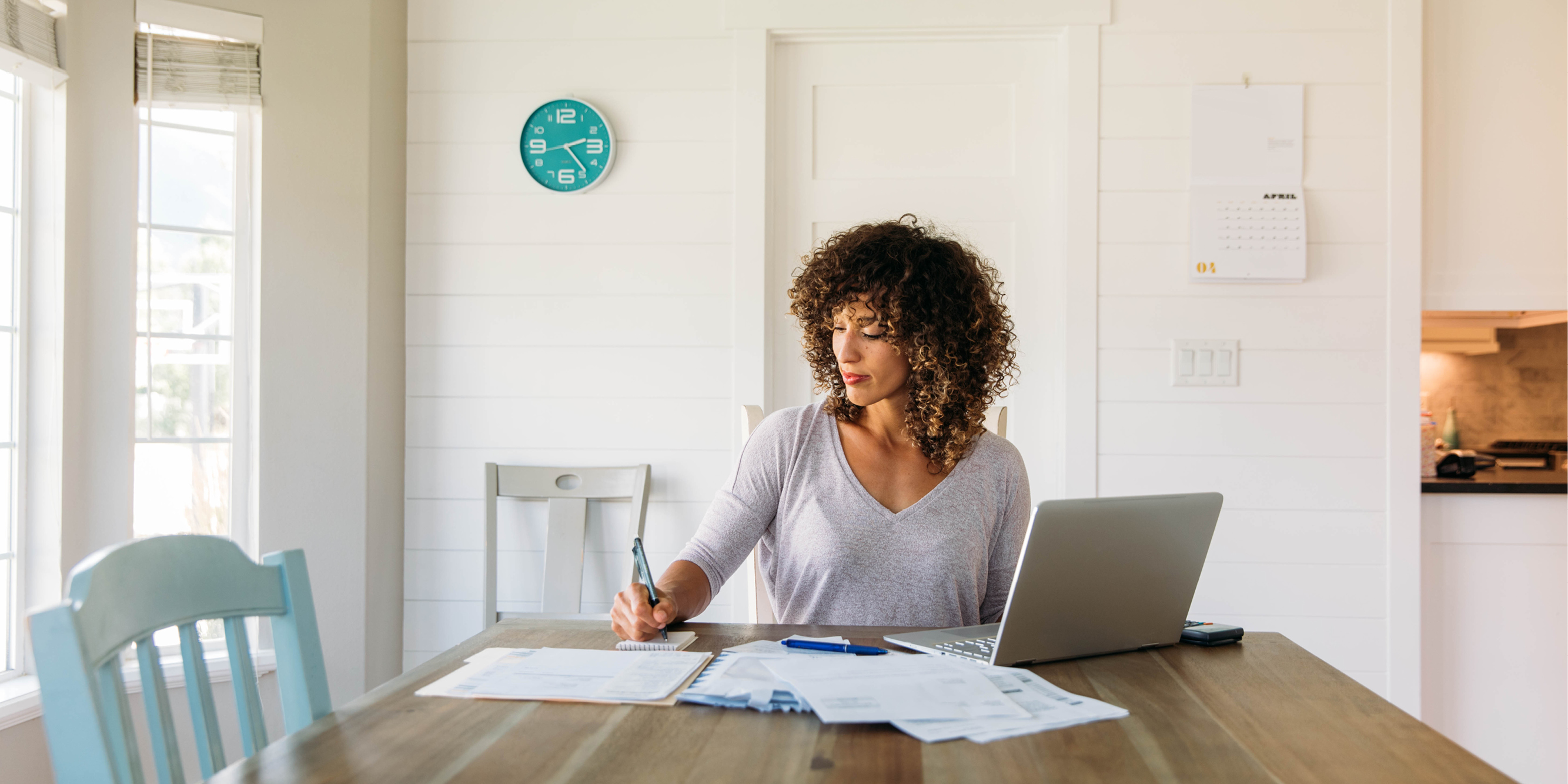 Woman completing paperwork while sitting at a kitchen table with a laptop