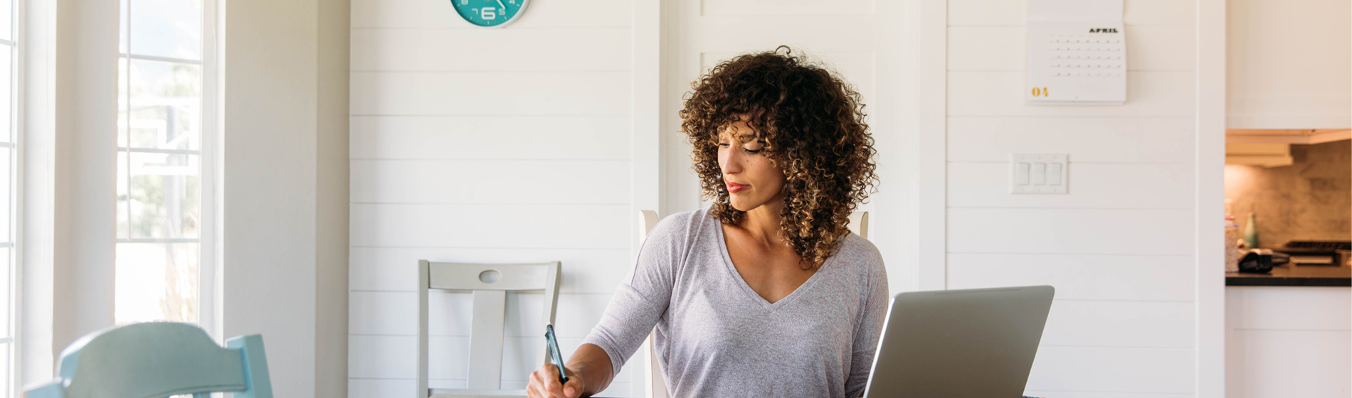 Woman completing paperwork while sitting at a kitchen table with a laptop