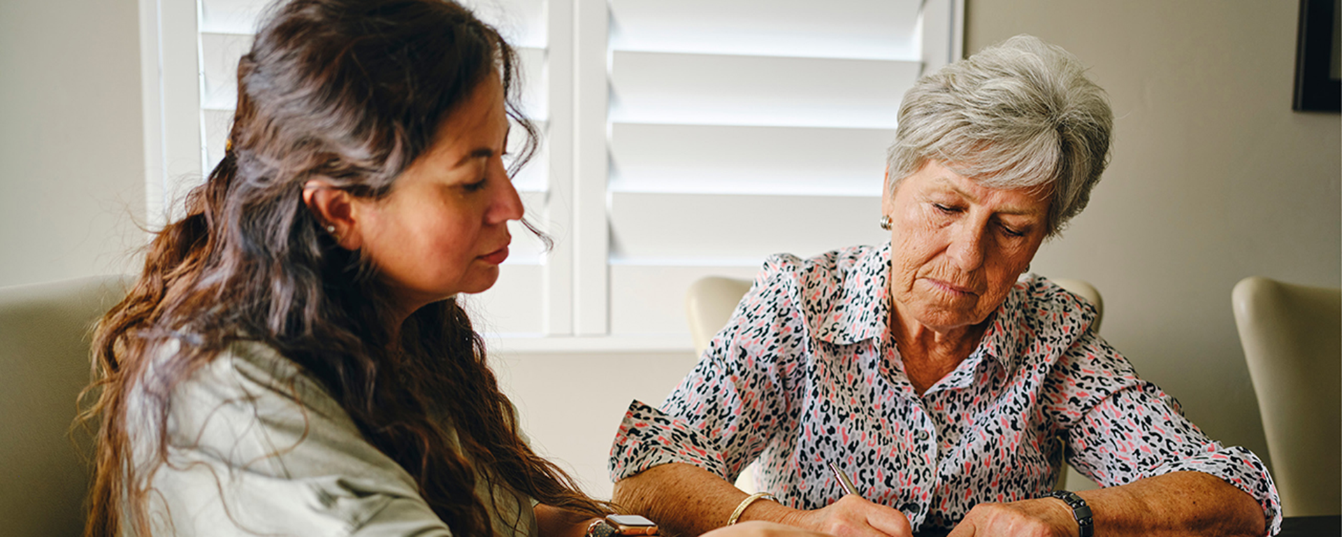 Adult at table with elderly parent looking at items on a table.