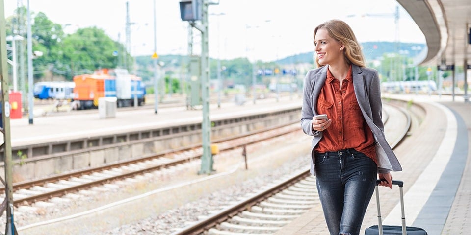 Blonde woman, smiling, while walking along train platform.