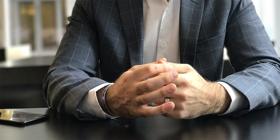 Faceless man, sitting at table with hands folded.