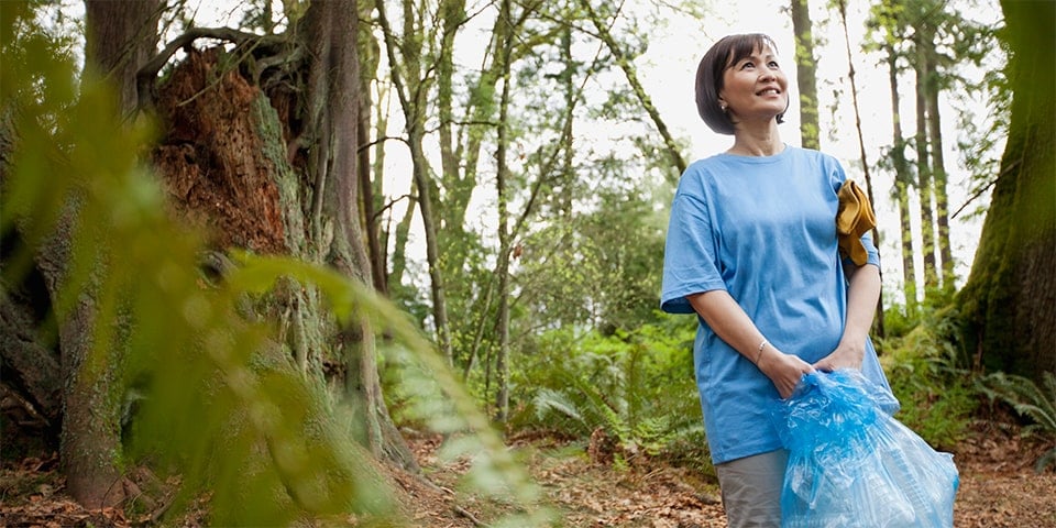 Asian-American female cleaning up trash from forest floor.