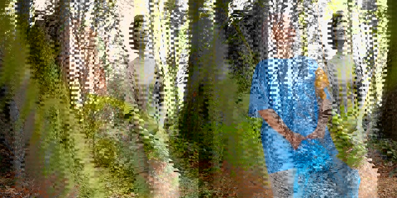 Asian-American female cleaning up trash from forest floor.