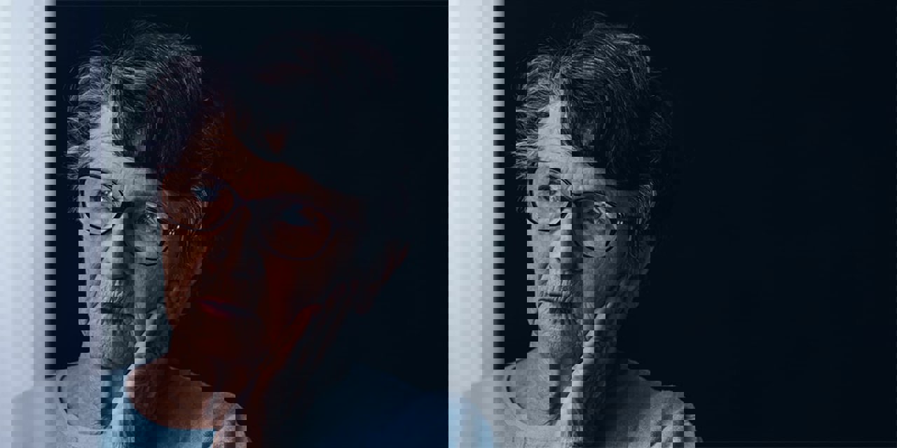 Worried, elderly woman with hand on face peering off into the distance.