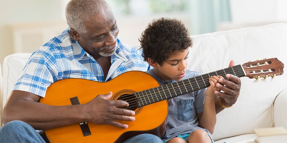 Grandfather teaching grandson how to play guitar.