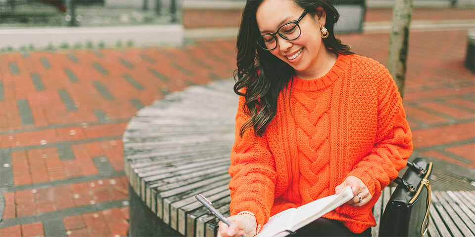 Young woman writing in notebook wearing an over-sized orange sweater.