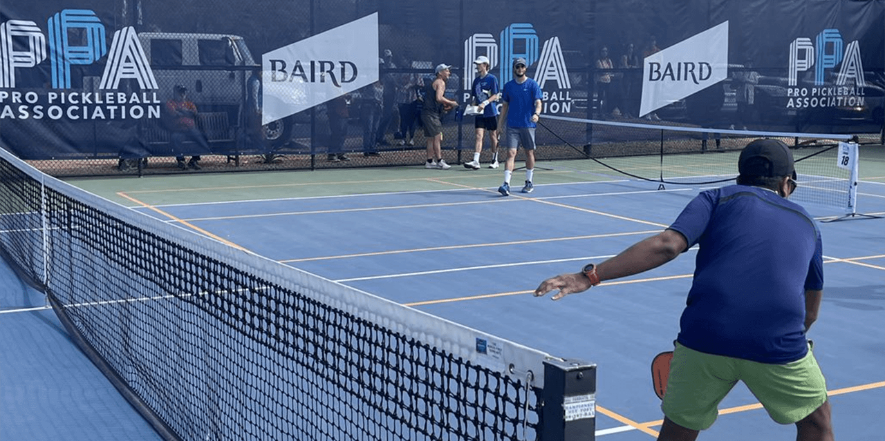 People playing pickleball on a large, outdoor court. Along the perimeter of of the court is a banner printed with the the Pro Pickleball Association and Baird logos.