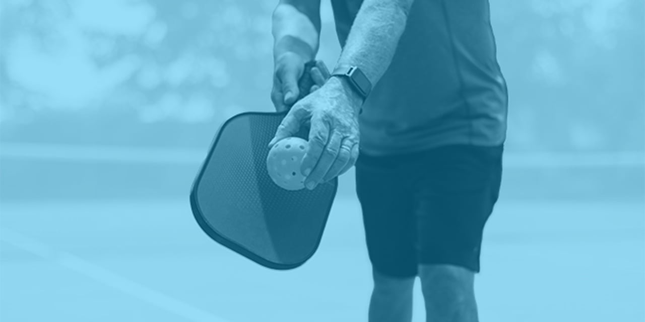 Man holding a pickleball paddle and ball