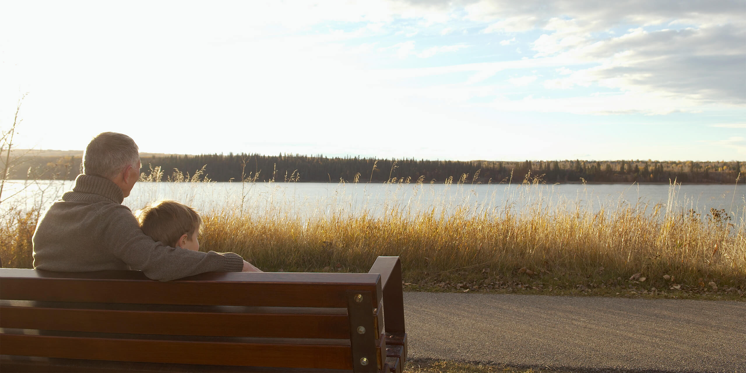 An older man and a young boy on a park bench looking out at a lake