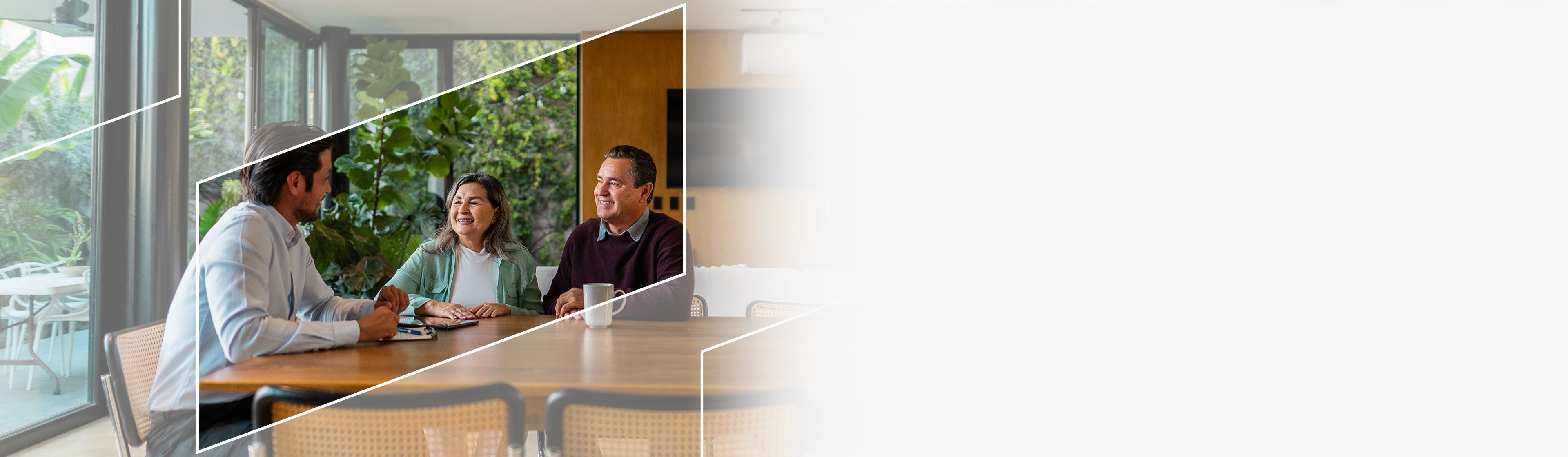 A financial advisor meeting with a couple at wooden table in a modern room with large windows and greenery outside
