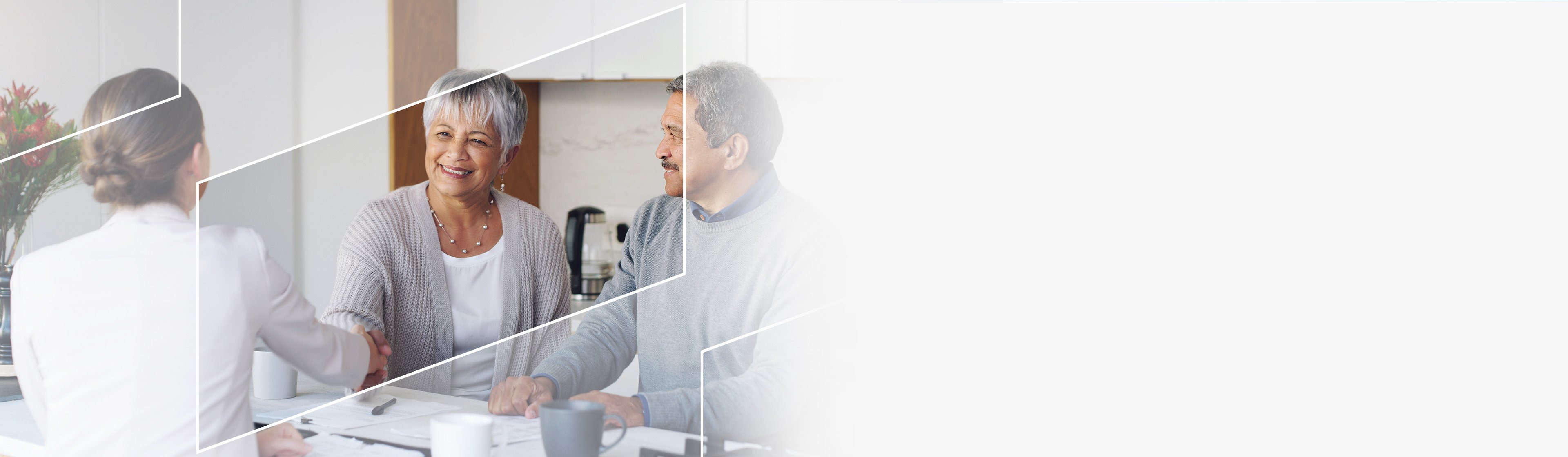 Two people meeting with a financial advisor at a table, shaking hands in a bright modern office setting