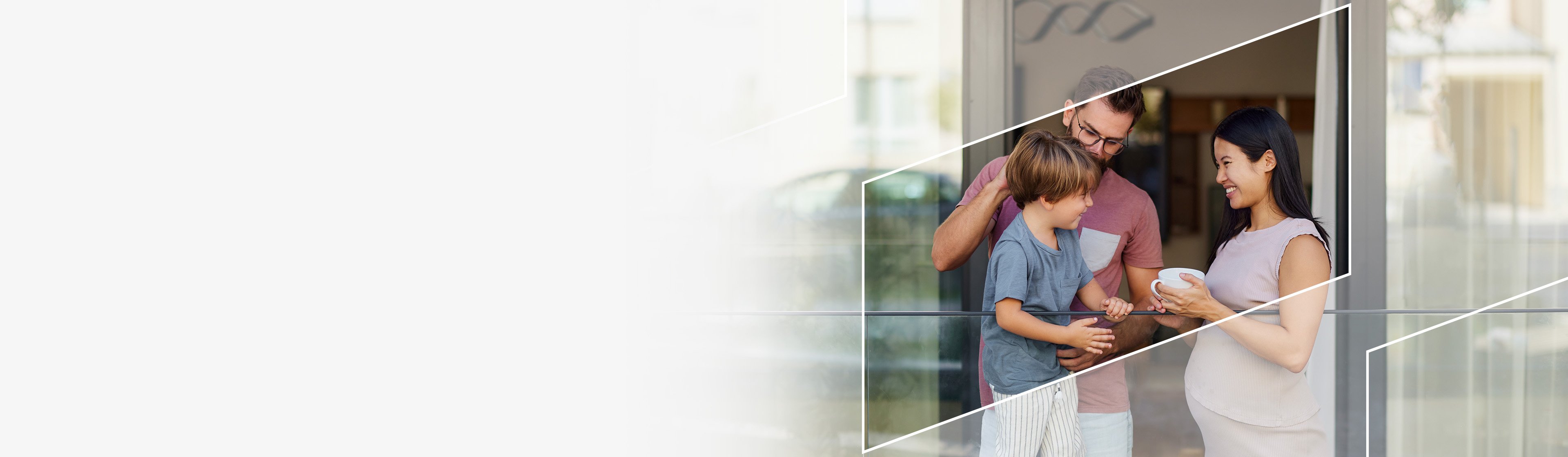 A family of three standing near a patio door, holding coffee cups and smiling
