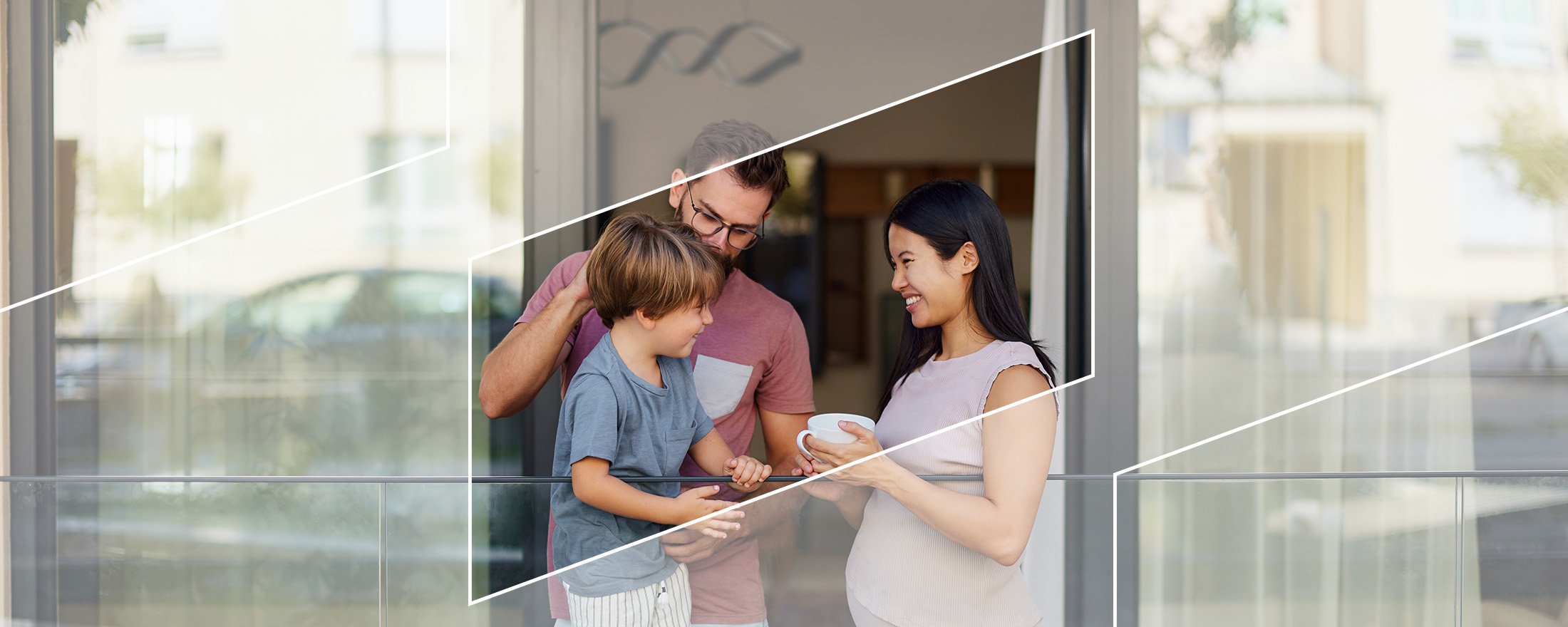 A family of three standing near a patio door, holding coffee cups and smiling