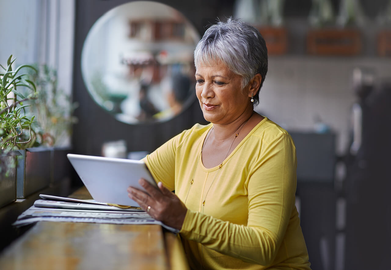 Woman sitting on a stool next to a newspaper looking at a tablet